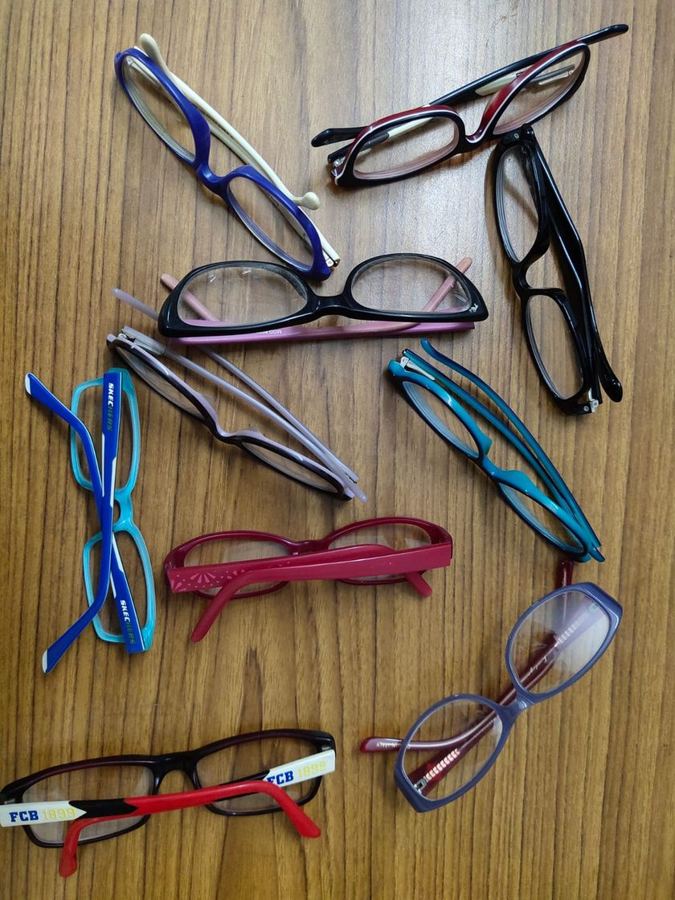 About a dozen children's and adults' glasses in blue, red and black laid out on a wooden table
